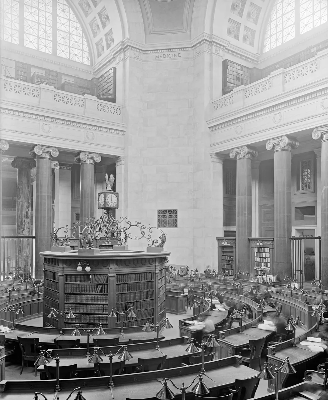 A black-and-white photograph of a domed reading room with tall columns, a round central desk and rows of curved reading tables.