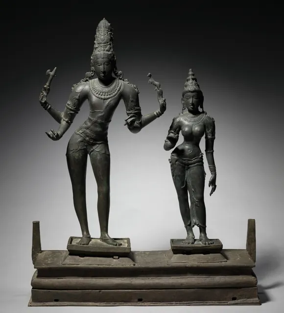 A bronze pair, four-armed Shiva and Parvati standing side by side on a shared stepped base with holes for the poles used to carry them in procession.