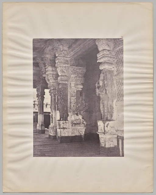 A sepia photograph of a row of massive carved stone pillars inside the Pudhu Mandapa hall at Madurai, mounted on a pale card.