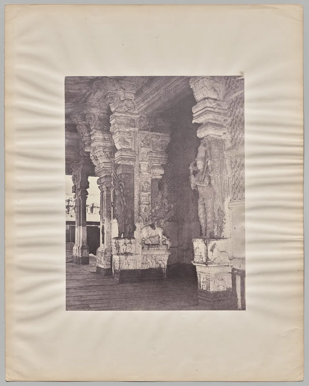 A sepia photograph of a row of massive carved stone pillars inside the Pudhu Mandapa hall at Madurai, mounted on a pale card.