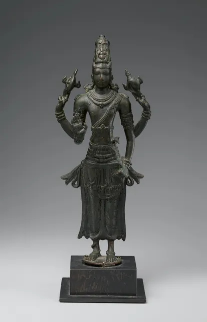 A small dark bronze of Vishnu standing straight on a square base, with four arms, the raised hands holding a wheel and a conch.