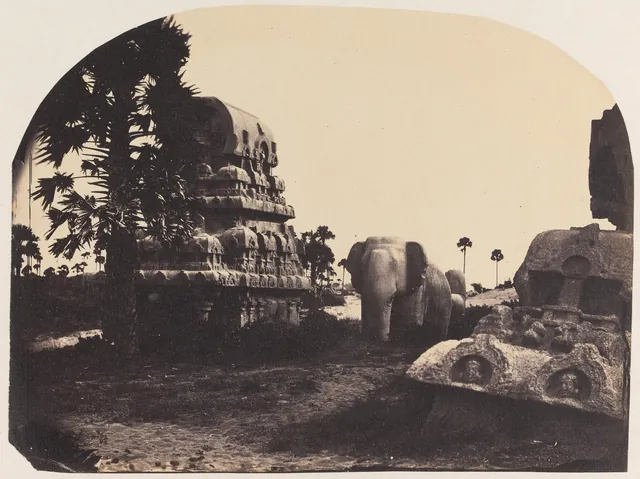 An 1858 photograph of a small Pallava shrine carved from a single granite boulder, with a stone elephant standing beside it under palm trees.